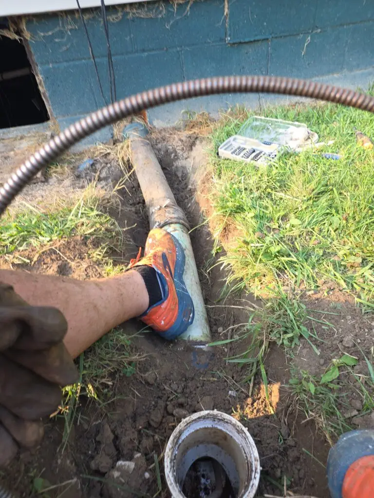 Drain cleaning cable and exposed PVC pipe in a shallow trench beside a foundation
