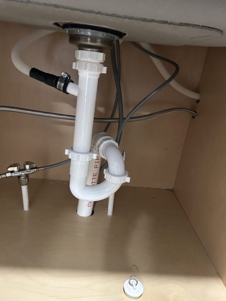 White PVC P-trap and supply lines under a residential sink cabinet