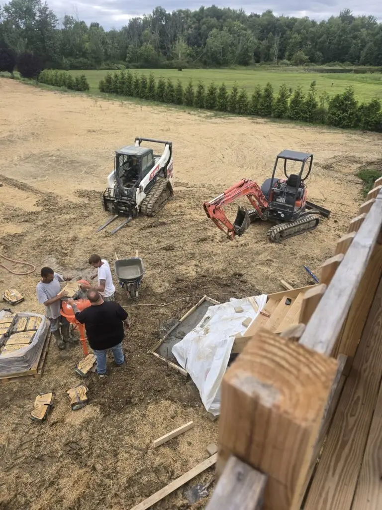 Crew with cement mixer, skid steer, and mini-excavator at a residential excavation site