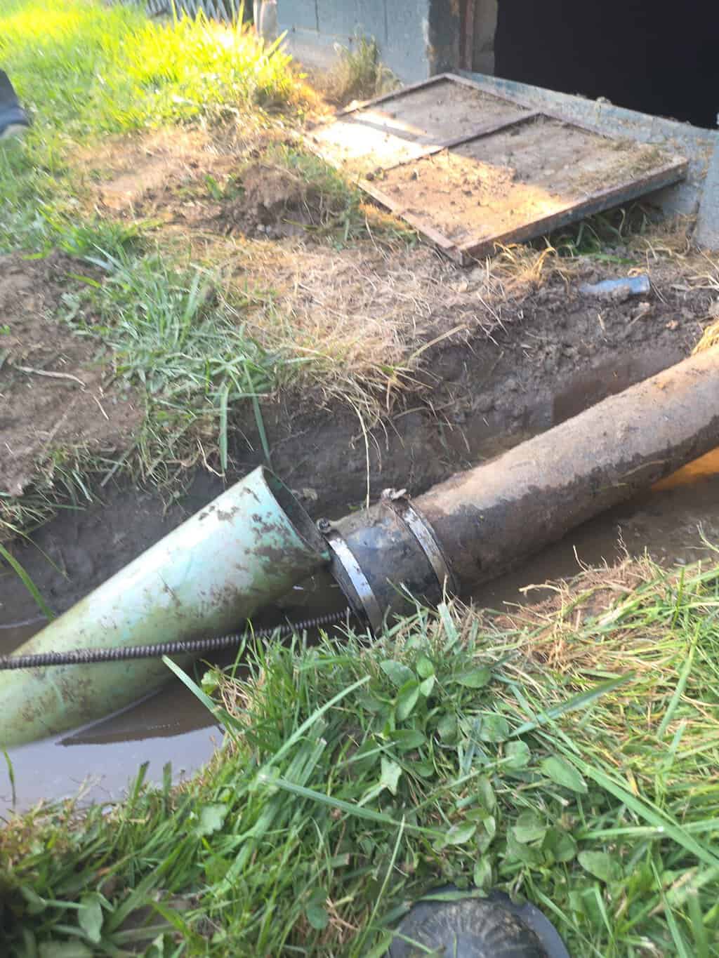 Green PVC pipe coupled to an older sewer line in a shallow outdoor trench