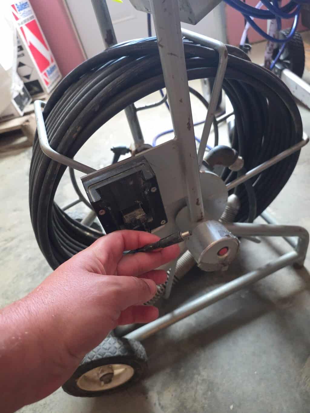 Technician connecting power to a wheeled sewer camera inspection cable reel