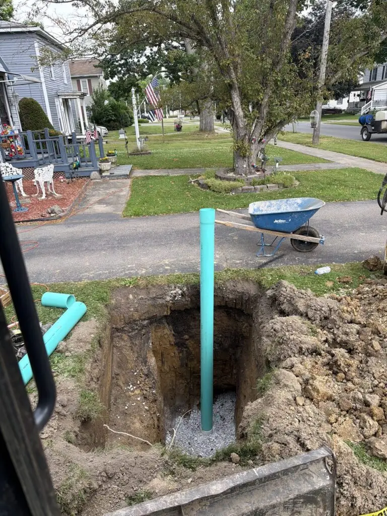 Excavated yard pit with a vertical sewer pipe set in gravel bedding