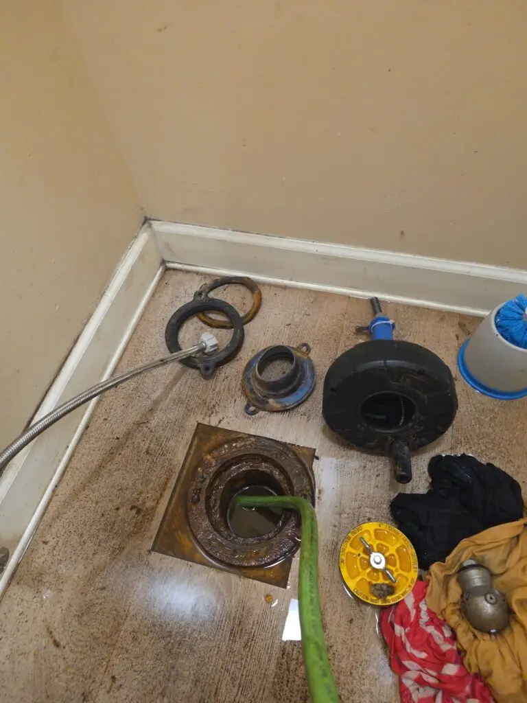 Green hydro-jetting hose inserted into an open floor drain with plumbing tools nearby