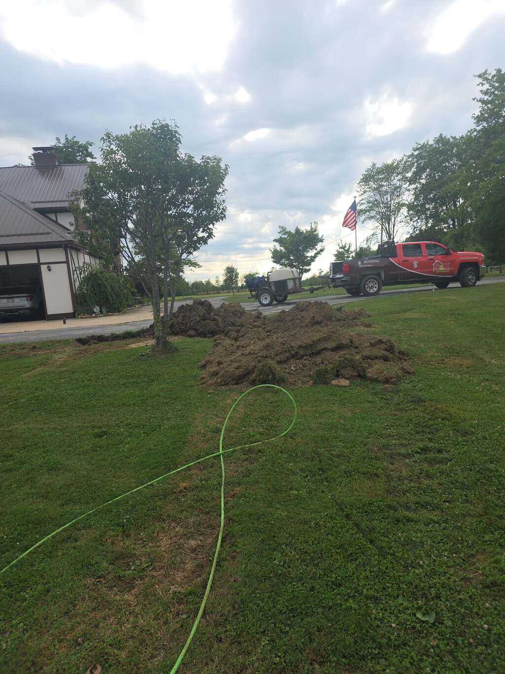 S&K Drain Cleaning service truck and tank trailer beside a residential yard excavation
