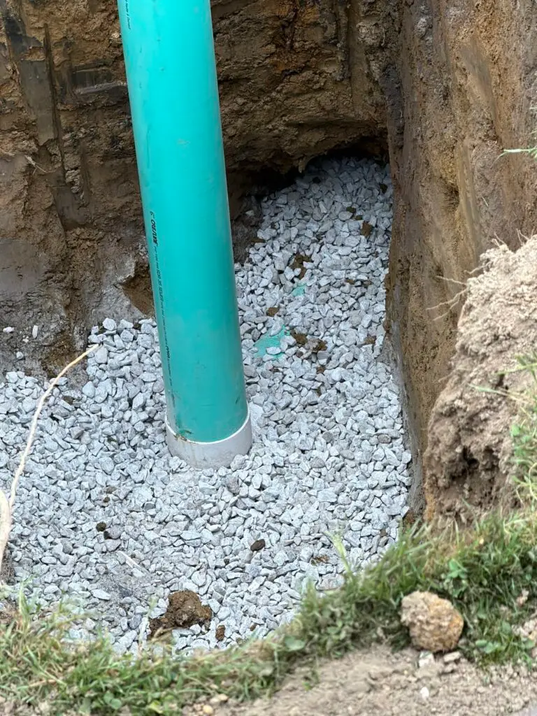 Vertical green PVC pipe standing in an excavated pit with gravel bedding