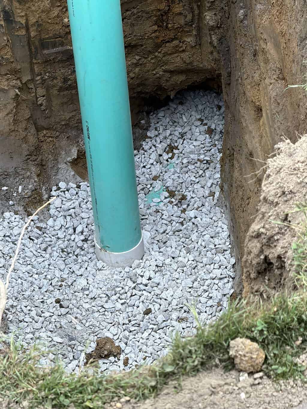 Vertical green PVC pipe standing in an excavated pit with gravel bedding