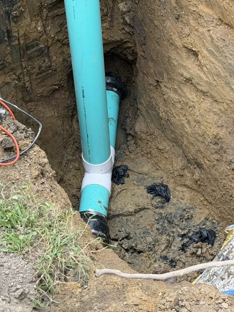 Light-blue PVC sewer piping with fittings installed in an excavated trench