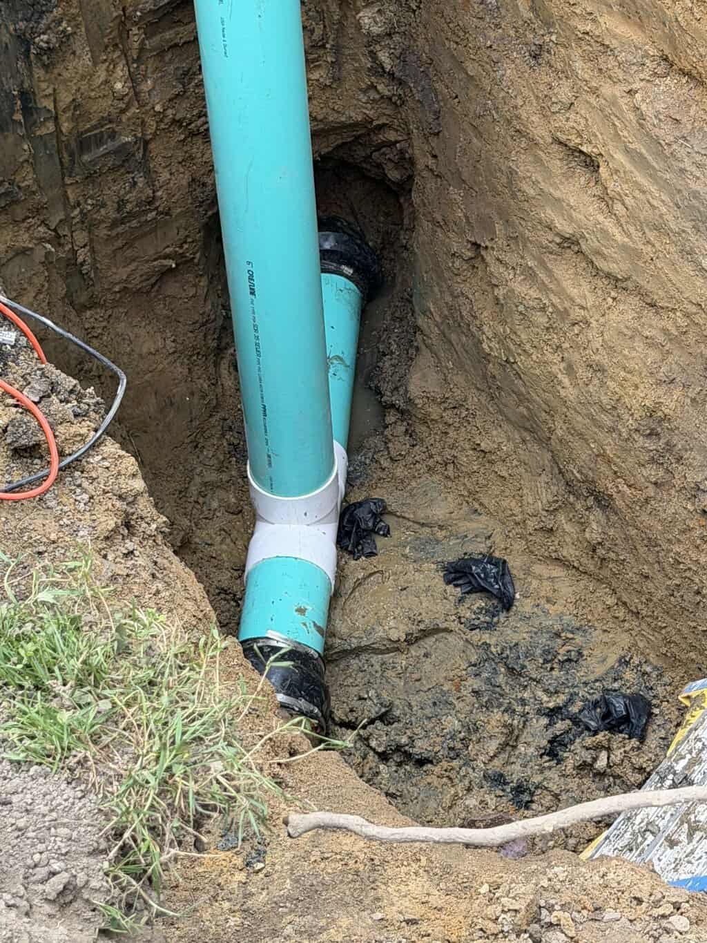 Light-blue PVC sewer piping with fittings installed in an excavated trench