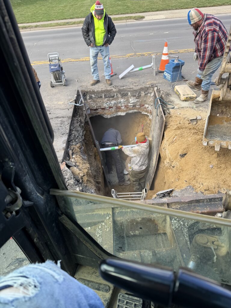 Workers inside a shored excavation pit during underground pipe repair