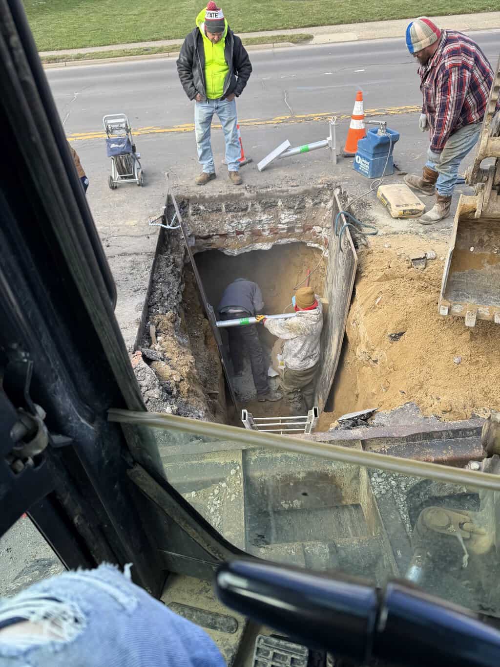 Workers inside a shored excavation pit during underground pipe repair