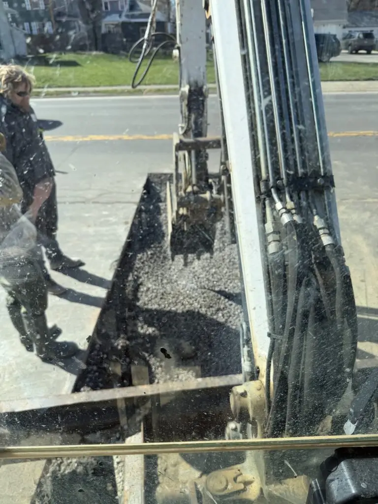 View from an excavator cab of a gravel-filled trench during underground pipe work